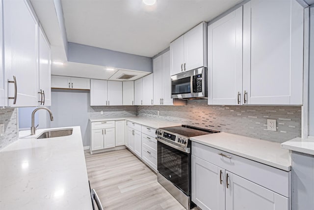 kitchen featuring sink, appliances with stainless steel finishes, white cabinetry, light stone countertops, and light wood-type flooring