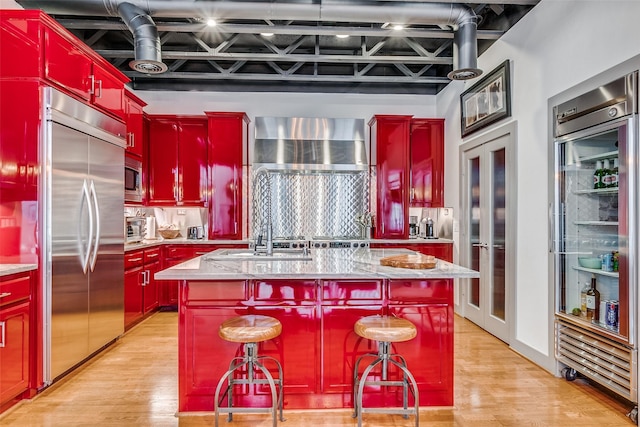 kitchen with light hardwood / wood-style flooring, a breakfast bar, built in appliances, light stone countertops, and a center island with sink