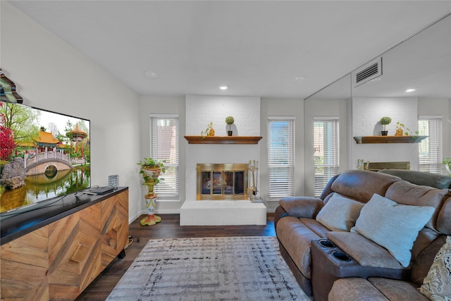 living room with a brick fireplace, dark wood-type flooring, and plenty of natural light