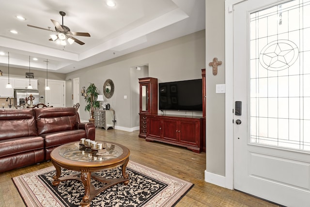 living room with hardwood / wood-style flooring, ceiling fan, a raised ceiling, and sink