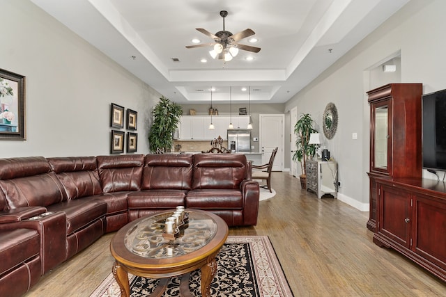 living room featuring ceiling fan, a tray ceiling, and light hardwood / wood-style floors