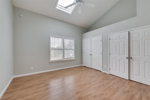 unfurnished bedroom featuring high vaulted ceiling, a skylight, ceiling fan, multiple closets, and light wood-type flooring