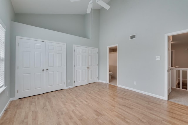 unfurnished bedroom with ceiling fan, high vaulted ceiling, connected bathroom, light hardwood / wood-style floors, and two closets