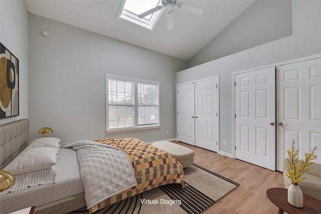 bedroom with high vaulted ceiling, a skylight, ceiling fan, light hardwood / wood-style floors, and multiple closets