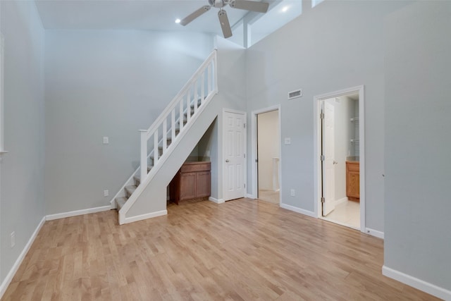 unfurnished living room featuring ceiling fan, a high ceiling, and light wood-type flooring