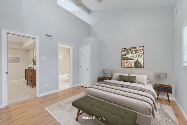 bedroom featuring ensuite bathroom, a towering ceiling, and light wood-type flooring