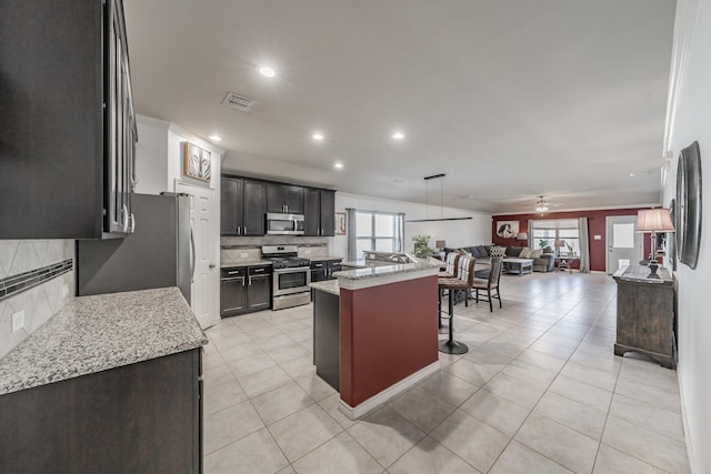 kitchen with appliances with stainless steel finishes, a kitchen island, light stone counters, a healthy amount of sunlight, and a kitchen bar