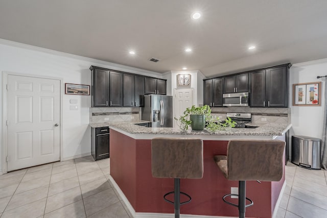 kitchen with light tile patterned floors, a breakfast bar area, stainless steel appliances, and a center island with sink