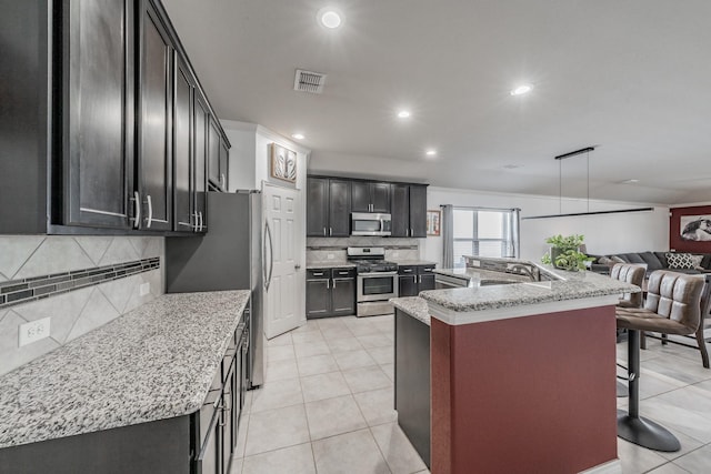 kitchen with an island with sink, a kitchen bar, light tile patterned floors, stainless steel appliances, and light stone countertops