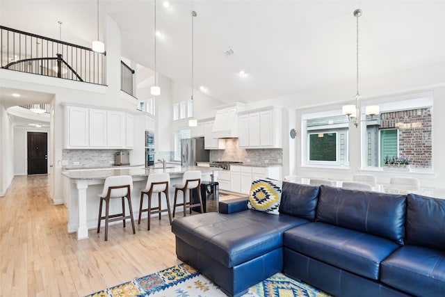 living room with a high ceiling, a wealth of natural light, a chandelier, and light hardwood / wood-style flooring