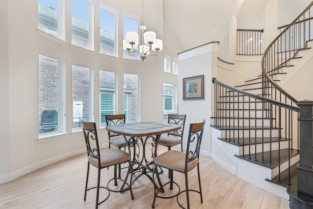 dining space featuring a towering ceiling, a notable chandelier, and light wood-type flooring