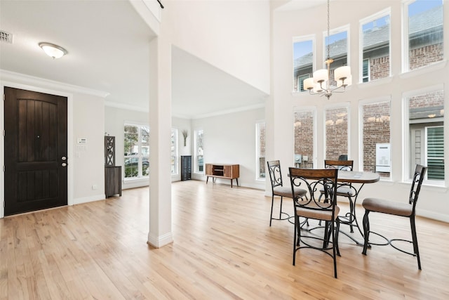 dining area featuring an inviting chandelier, ornamental molding, a high ceiling, and light wood-type flooring