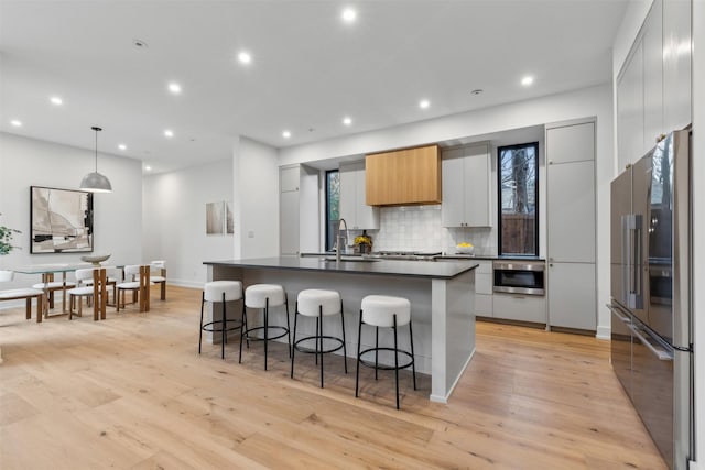 kitchen featuring sink, decorative light fixtures, high quality fridge, a kitchen island with sink, and light hardwood / wood-style floors