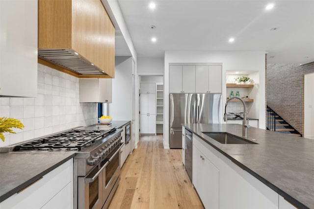 kitchen with premium range hood, sink, white cabinetry, appliances with stainless steel finishes, and light hardwood / wood-style floors