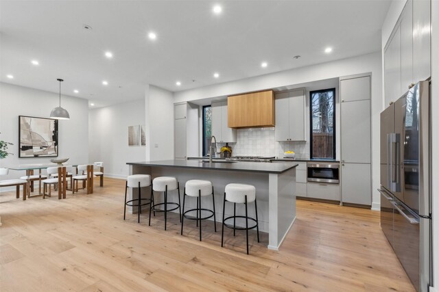 kitchen with dark countertops, appliances with stainless steel finishes, a sink, light wood finished floors, and decorative backsplash
