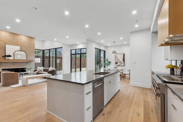 kitchen featuring decorative light fixtures, white cabinetry, sink, stainless steel appliances, and a brick fireplace