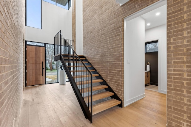 staircase with hardwood / wood-style flooring, brick wall, and a high ceiling