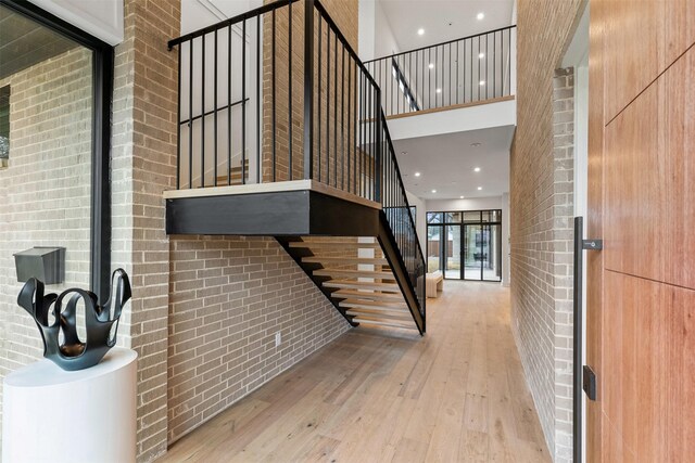 stairway featuring wood-type flooring, a towering ceiling, and brick wall