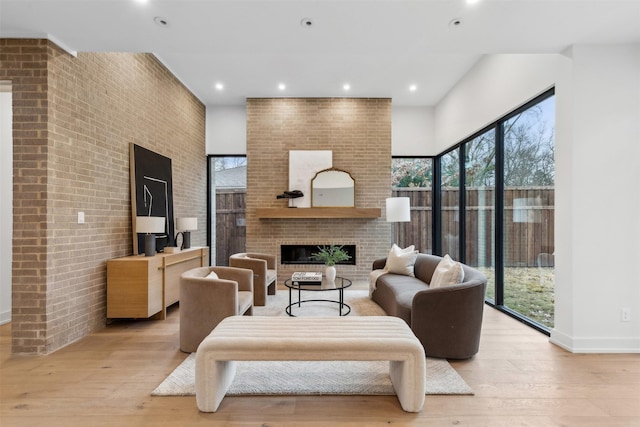 living room with brick wall, a wealth of natural light, a brick fireplace, and light hardwood / wood-style flooring