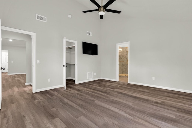 unfurnished bedroom with dark wood-type flooring, ceiling fan, a towering ceiling, a walk in closet, and a closet