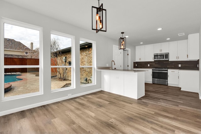 kitchen featuring white cabinetry, sink, backsplash, hanging light fixtures, and stainless steel appliances