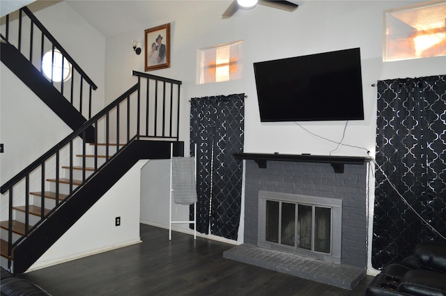 stairway featuring ceiling fan, hardwood / wood-style floors, a brick fireplace, and a towering ceiling