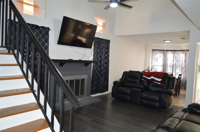 living room featuring hardwood / wood-style flooring, ceiling fan, a brick fireplace, and a high ceiling