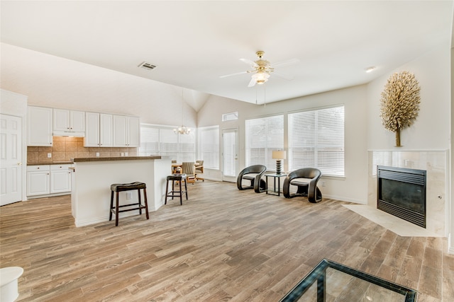 living room featuring ceiling fan with notable chandelier, a fireplace, high vaulted ceiling, and light wood-type flooring