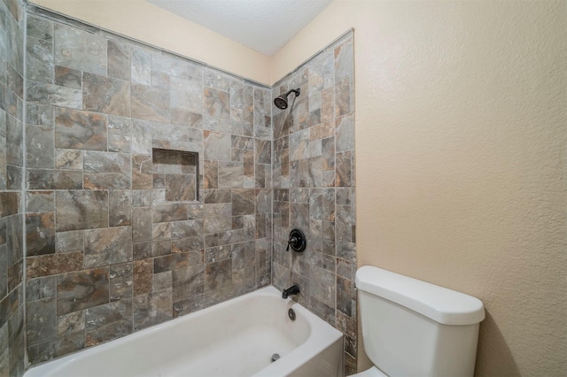 bathroom featuring a textured ceiling, toilet, and tiled shower / bath