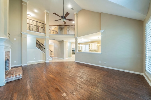 unfurnished living room with ceiling fan, wood-type flooring, a fireplace, and decorative columns