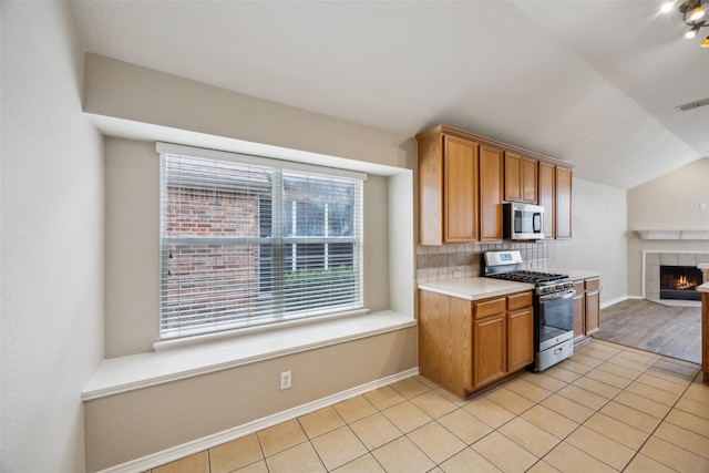 kitchen with tasteful backsplash, stainless steel appliances, a tiled fireplace, and light tile patterned floors