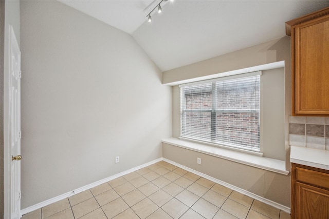 unfurnished dining area featuring track lighting, lofted ceiling, and light tile patterned floors