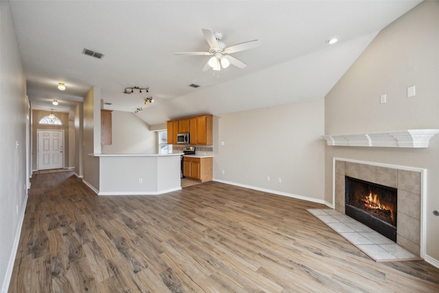 unfurnished living room featuring a tiled fireplace, vaulted ceiling, ceiling fan, and light wood-type flooring