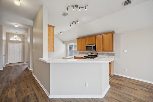 kitchen with lofted ceiling, dark wood-type flooring, appliances with stainless steel finishes, backsplash, and kitchen peninsula