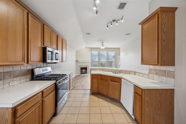 kitchen featuring appliances with stainless steel finishes, sink, decorative backsplash, light tile patterned floors, and kitchen peninsula