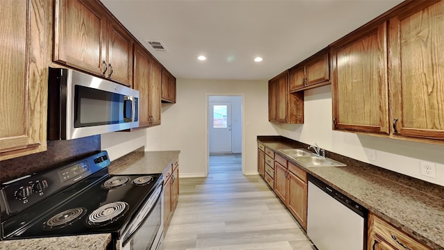 kitchen with sink, light hardwood / wood-style flooring, dark stone counters, and appliances with stainless steel finishes