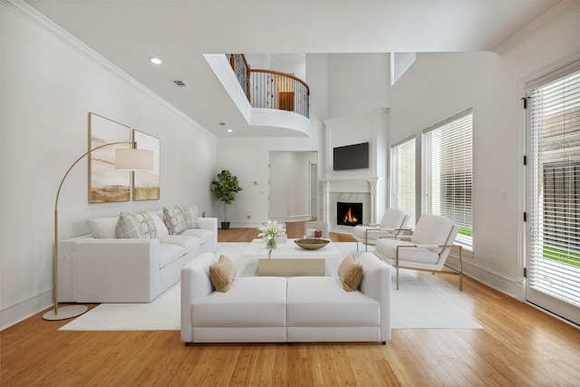 living room with a fireplace, a towering ceiling, light hardwood / wood-style flooring, and ornamental molding