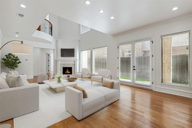 living room featuring a high ceiling, ornamental molding, light wood-type flooring, and a fireplace