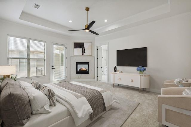 bedroom with ceiling fan, light colored carpet, a high end fireplace, and a tray ceiling