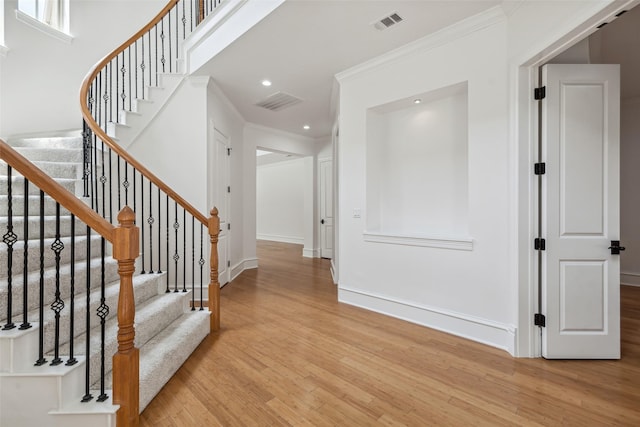 foyer entrance featuring crown molding, light hardwood / wood-style flooring, and a high ceiling