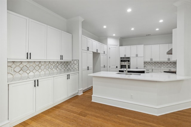 kitchen with sink, white cabinets, double oven, and light wood-type flooring