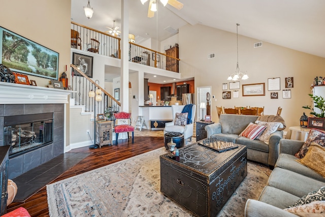 living room with hardwood / wood-style flooring, vaulted ceiling, a tiled fireplace, and ceiling fan with notable chandelier