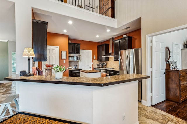 kitchen with stainless steel appliances, tasteful backsplash, wall chimney range hood, and kitchen peninsula