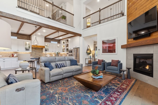 living room featuring hardwood / wood-style flooring, a tiled fireplace, a towering ceiling, and beamed ceiling