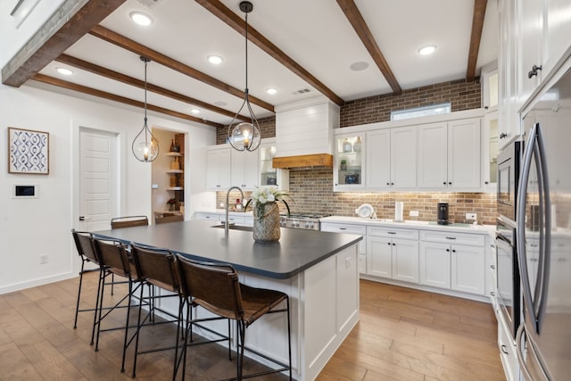 kitchen featuring pendant lighting, a kitchen island with sink, custom range hood, and white cabinets