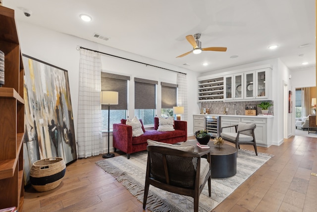 living room with wet bar, light hardwood / wood-style floors, beverage cooler, and ceiling fan