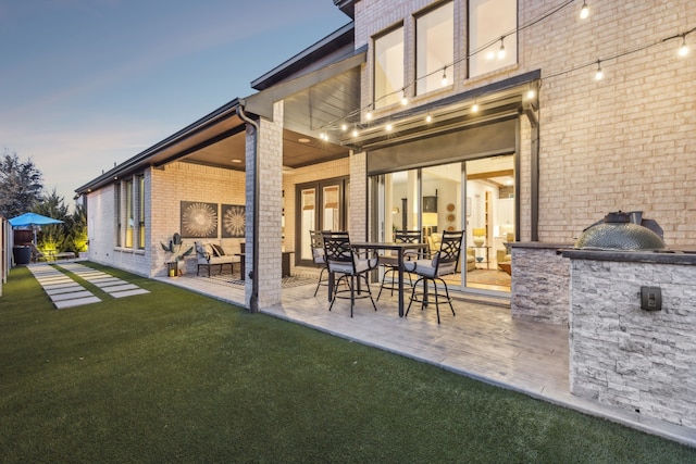 back house at dusk with exterior kitchen, a patio, and a yard