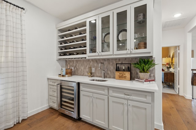 bar with wood-type flooring, sink, wine cooler, and backsplash