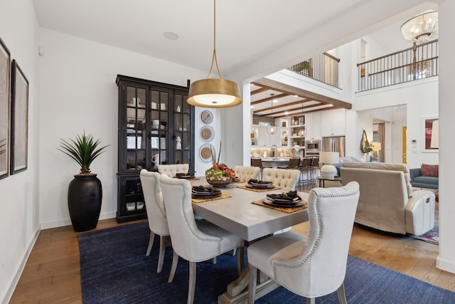 dining space with a high ceiling, a chandelier, light hardwood / wood-style floors, and beam ceiling