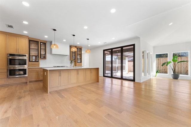 kitchen featuring light wood-type flooring, plenty of natural light, pendant lighting, stainless steel double oven, and a kitchen island with sink